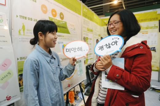굿네이버스의 '학교폭력 예방교육' 부스에서 두 여학생이 말풍선을 들어보이며 대화하고 있다.