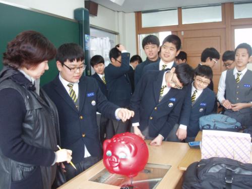 학생들이 빨간 돼지저금통에 동전을 넣고 있다.