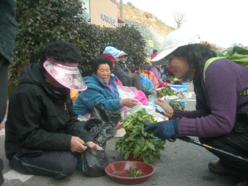 마을 아낙네에게 냉이와 시금치를 사고 있다.